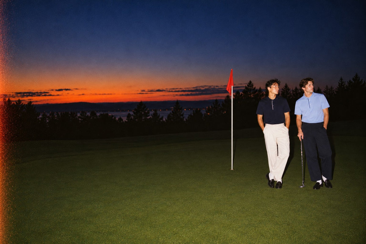 Two men in Arca Fairway Polos (navy and light blue) on a green at dusk